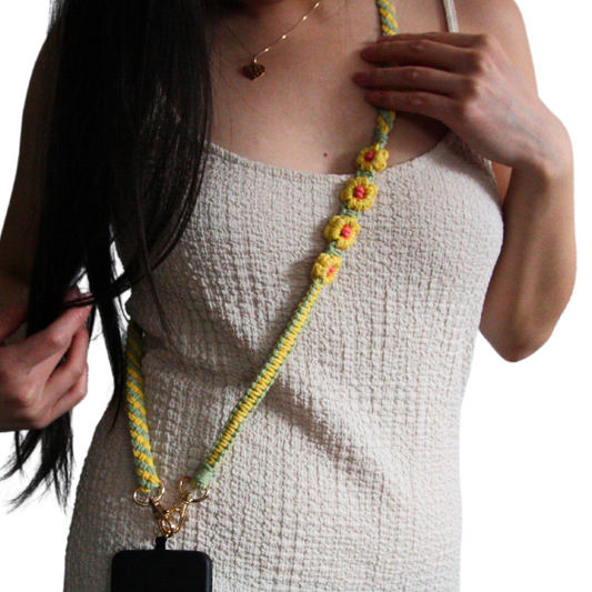 Girl wearing white dress and posing with her yellow and green crossbody phone strap with flowers.