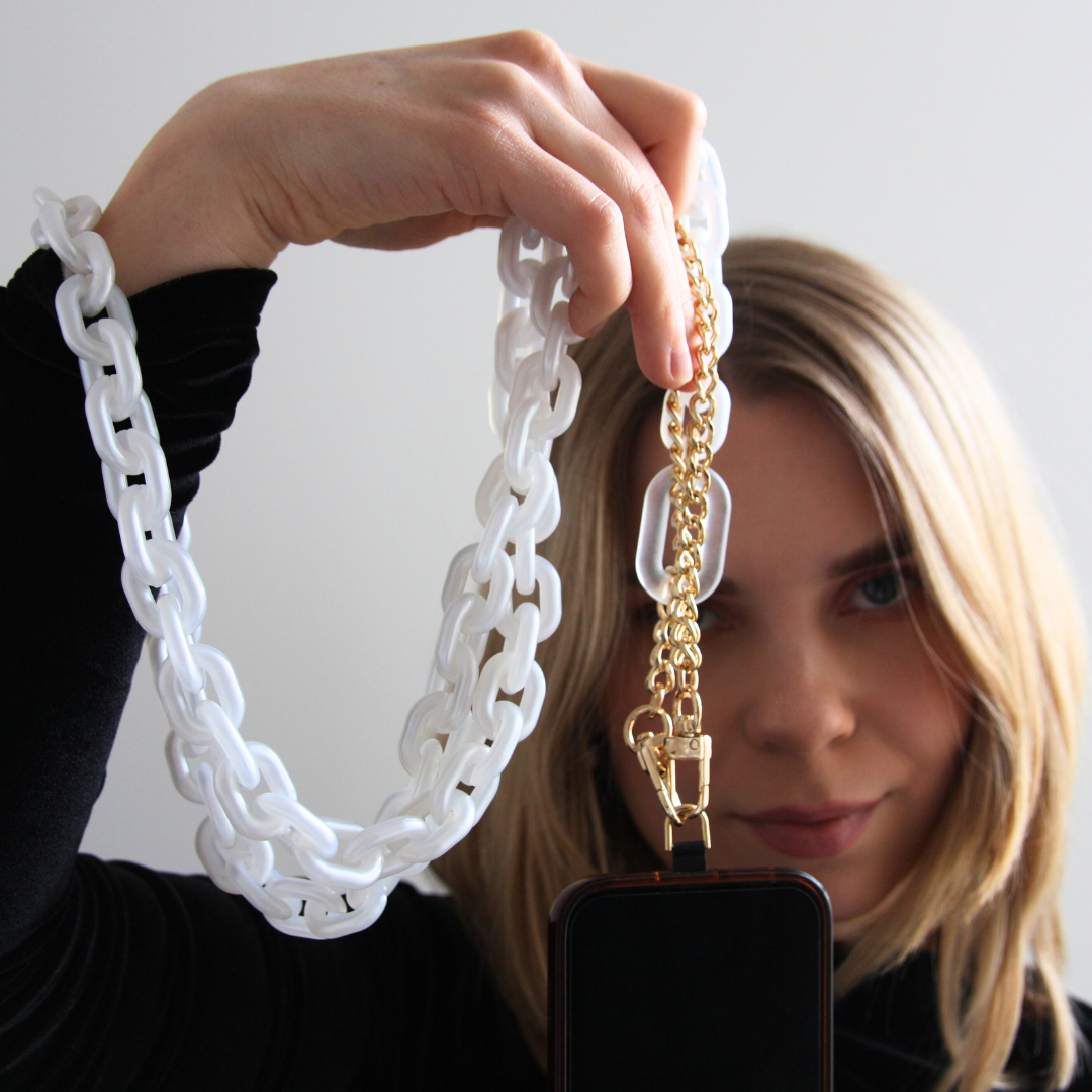 Blond girl holding white chain crossbody phone strap with a gold touch.