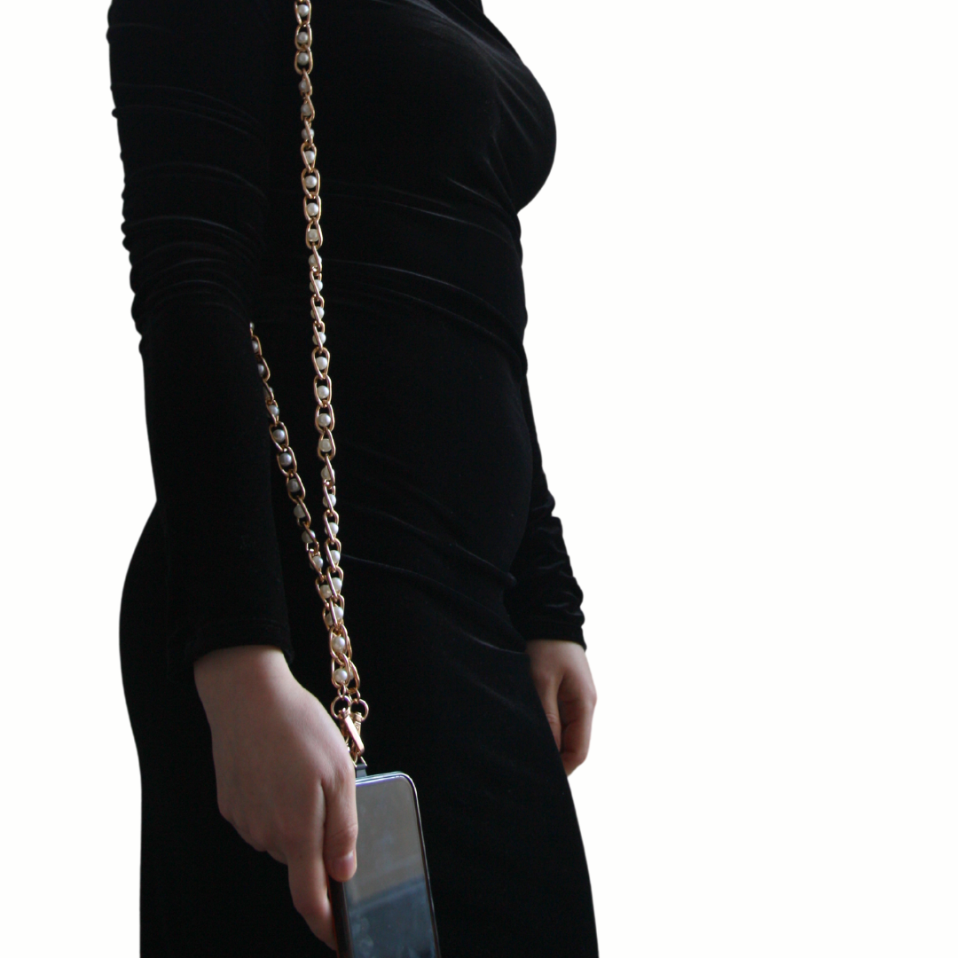 Girl with long black dress wearing a white and golden crossbody phone strap.