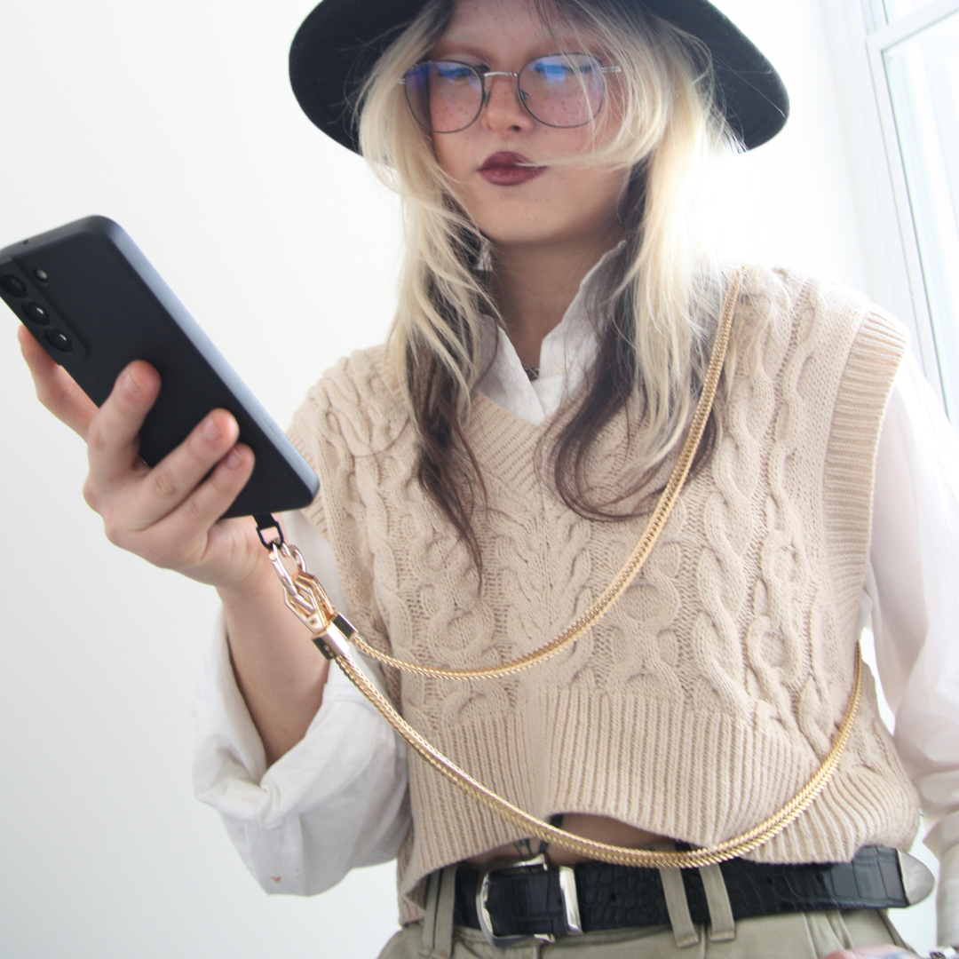 Girl looking at her phone. Wearing golden crossbody phone strap.