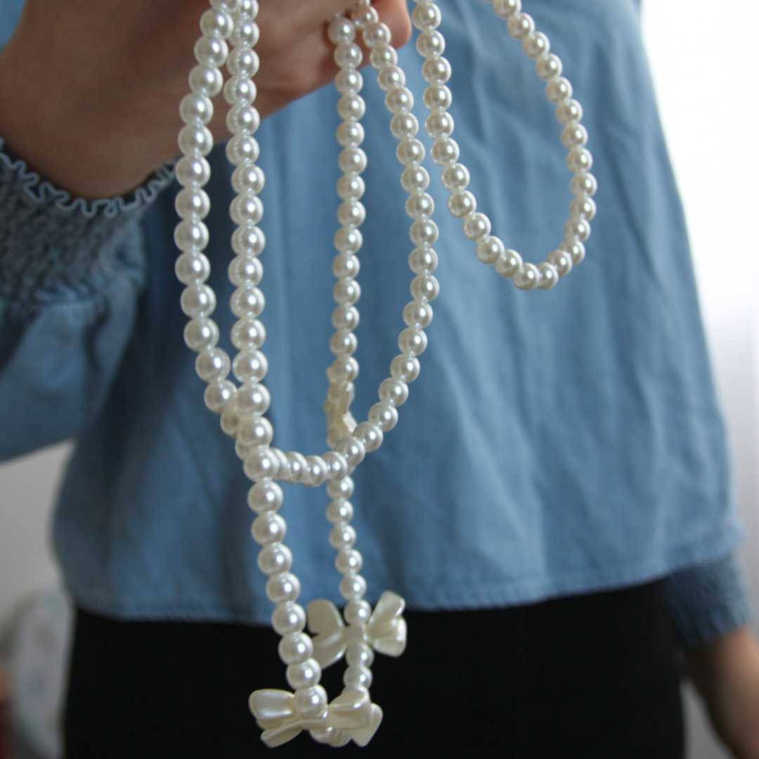 Close-up photo of the white crossbody phone strap with pearls and bows.