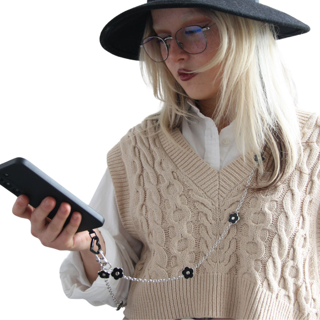 Girl with blond hair holding her phone. Wearing the black and silver flower crossbody phone strap.