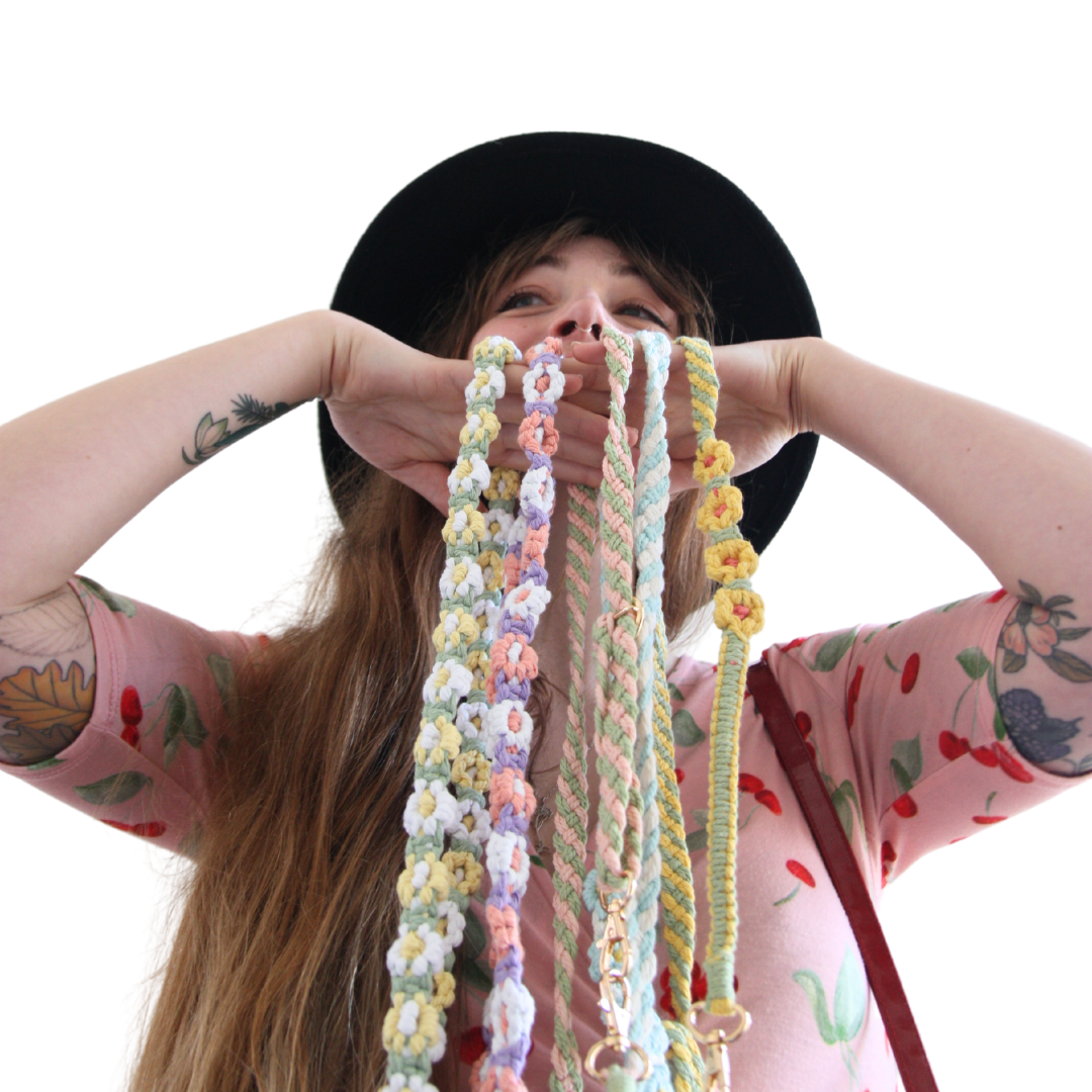 Girl with brown hair holding five different crossbody phone straps with flowers in front of her face.