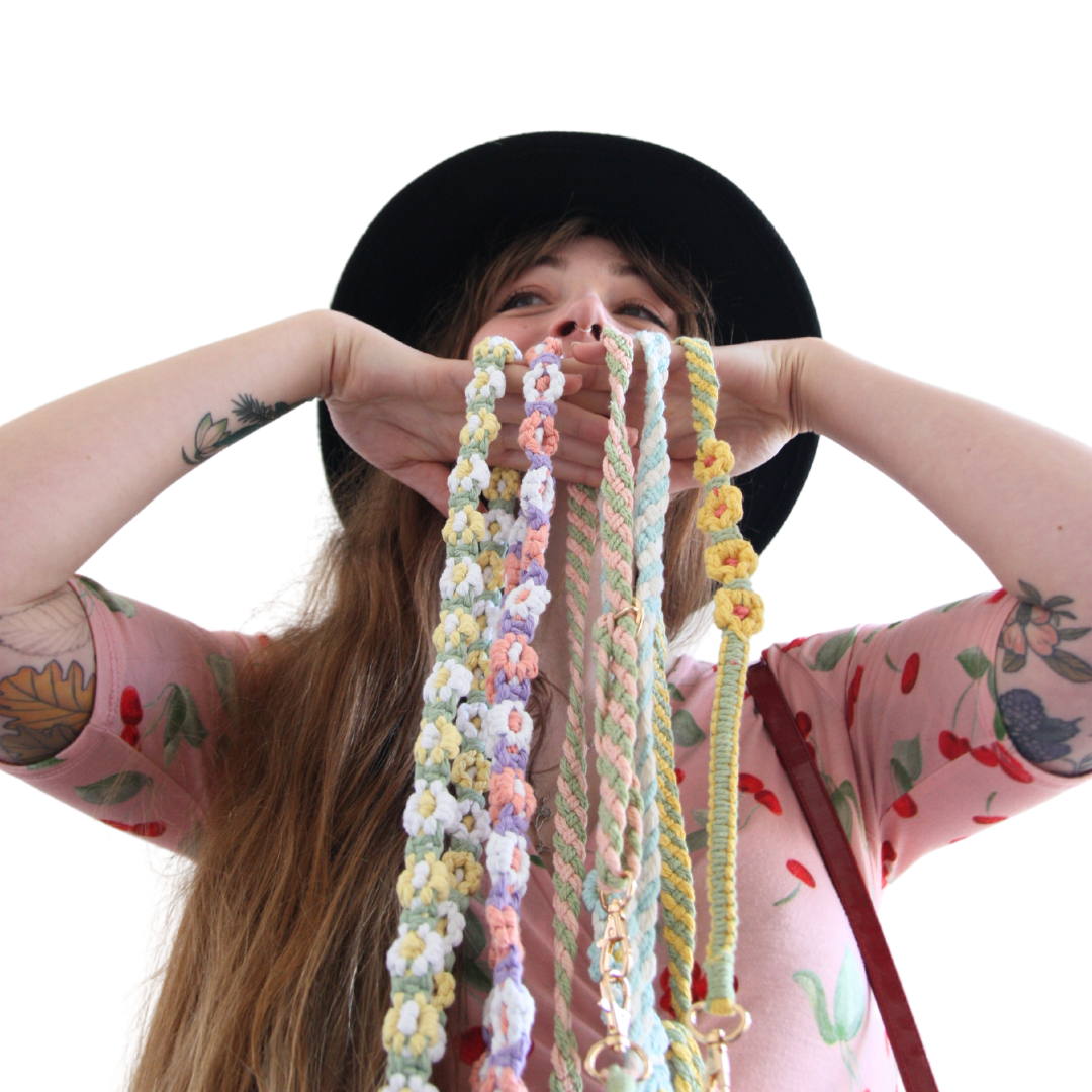 Girl with long brown hair holding five different coloured crossbody phone straps with flowers.