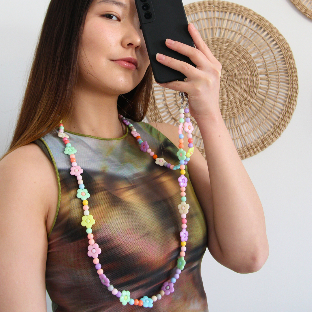 Asian girl holding her phone in front of one eye. Wearing the multicoloured beads crossbody phone strap.