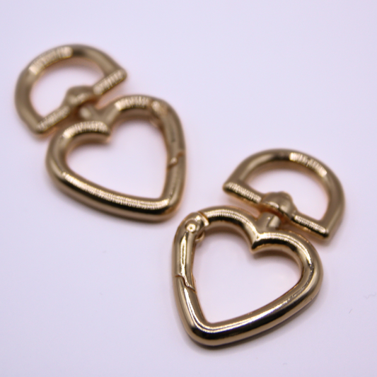 Plain background. Two double gold heart shaped carabiners in front.